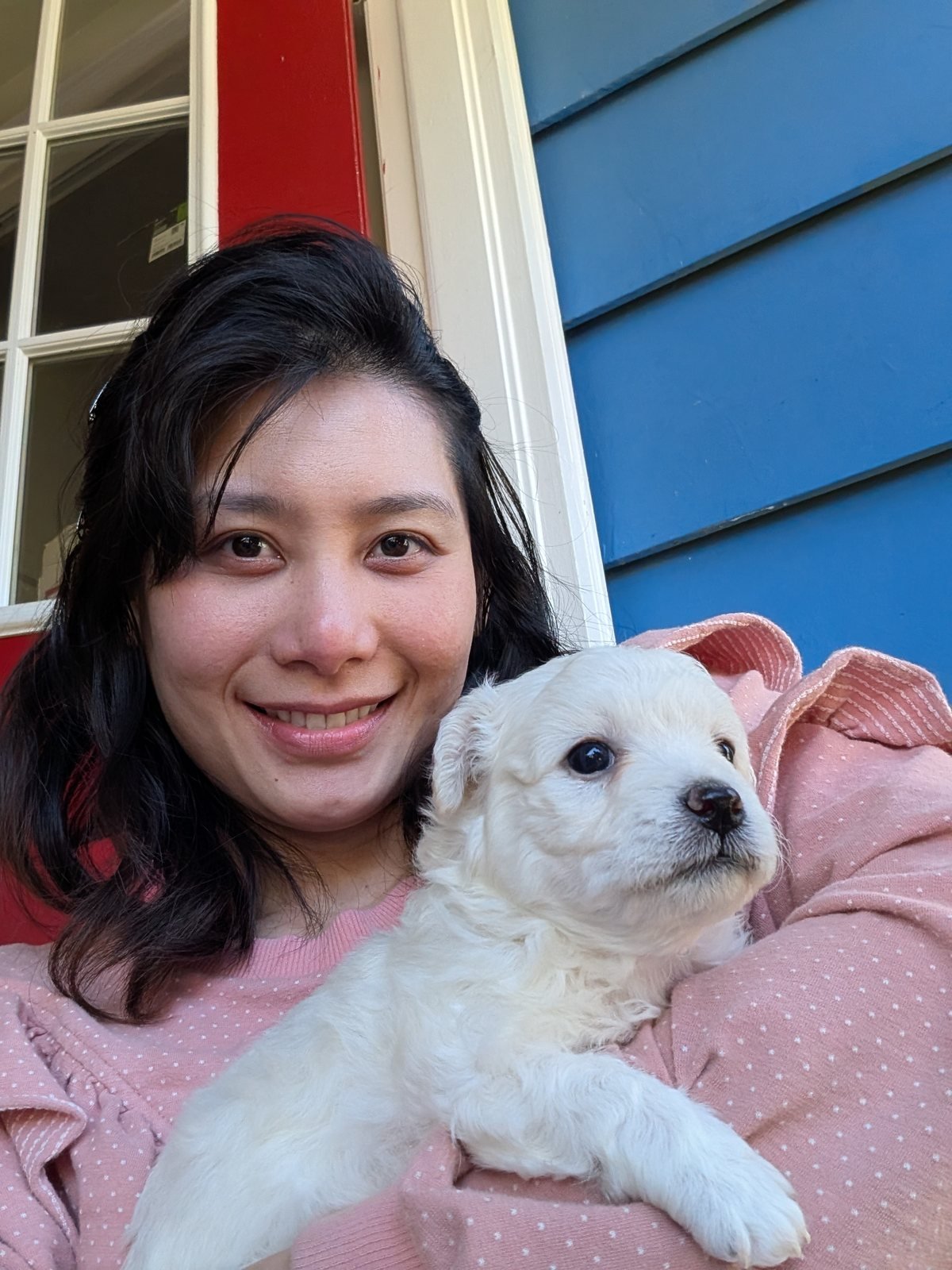 Me in a pink top holding a white puppy in front of a red door
